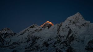 Mountain peaks glowing in golden sunset light with snow-covered slopes in shadow.