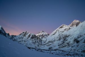 Snow-capped mountain peaks against a dark blue sky at dusk in a dramatic panoramic landscape.