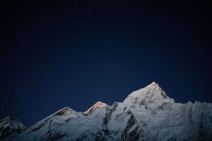 Jagged mountain ridges covered in snow silhouetted against a deep blue evening sky.