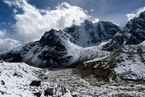 Dramatic mountain landscape with snow-covered peaks and glaciers under bright clouds.