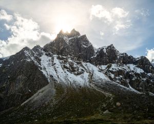 Jagged snow-covered mountain peaks rise against a bright blue sky with white clouds.