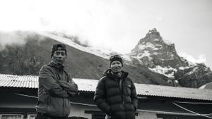 Silhouettes of hikers stand against a dramatic mountain backdrop in black and white.