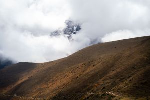 Misty mountain slopes fade into clouds with snow-capped peaks visible in the distance.