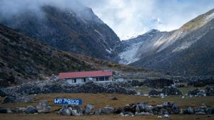 Small buildings and structures dot the base of towering snow-covered mountains in a remote valley.