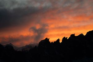 Silhouetted mountain ridges against a fiery orange sunset sky creating a dramatic mountain landscape.