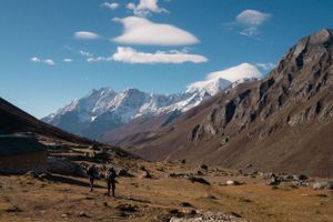 Rocky mountain trail with snow-capped peaks in the distance under blue skies.