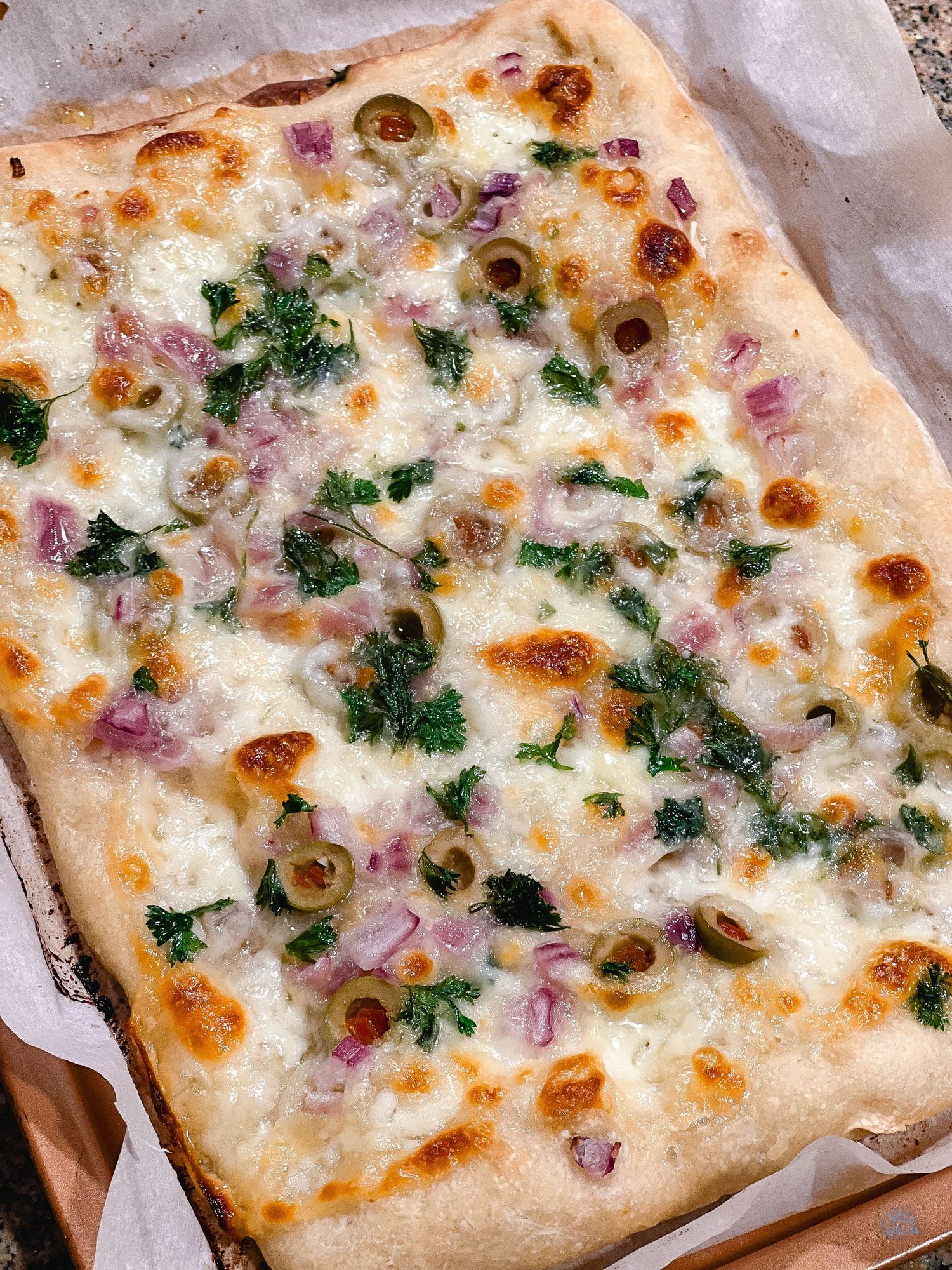 White pizza topped with melted cheese, red onions, olives and fresh herbs.