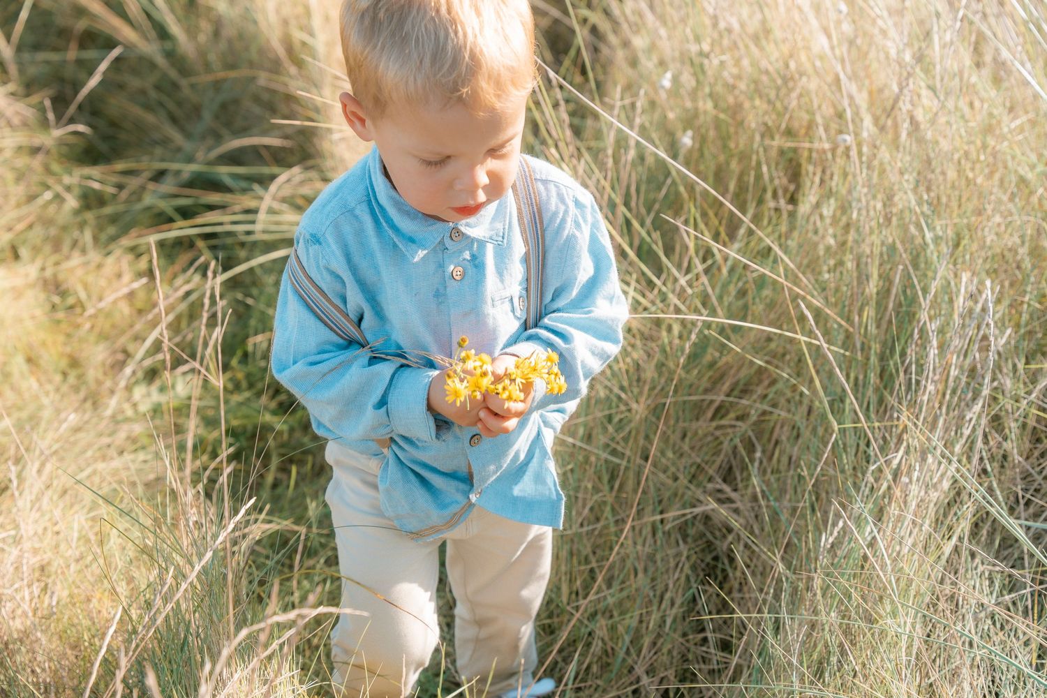 Small child in light blue sweater explores outdoors while holding something.