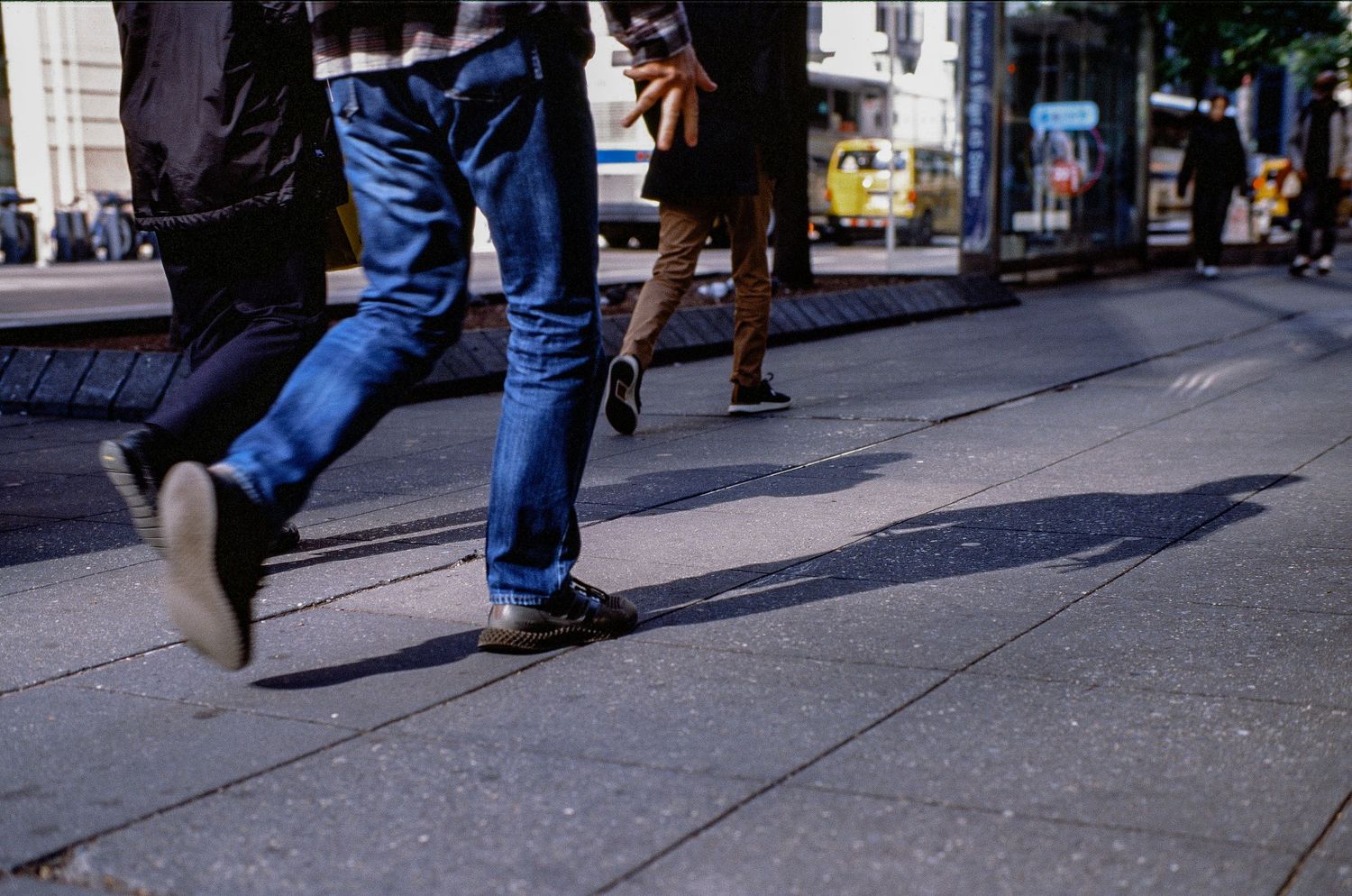 Urban street scene showing walking feet and legs in blue jeans on a city sidewalk.