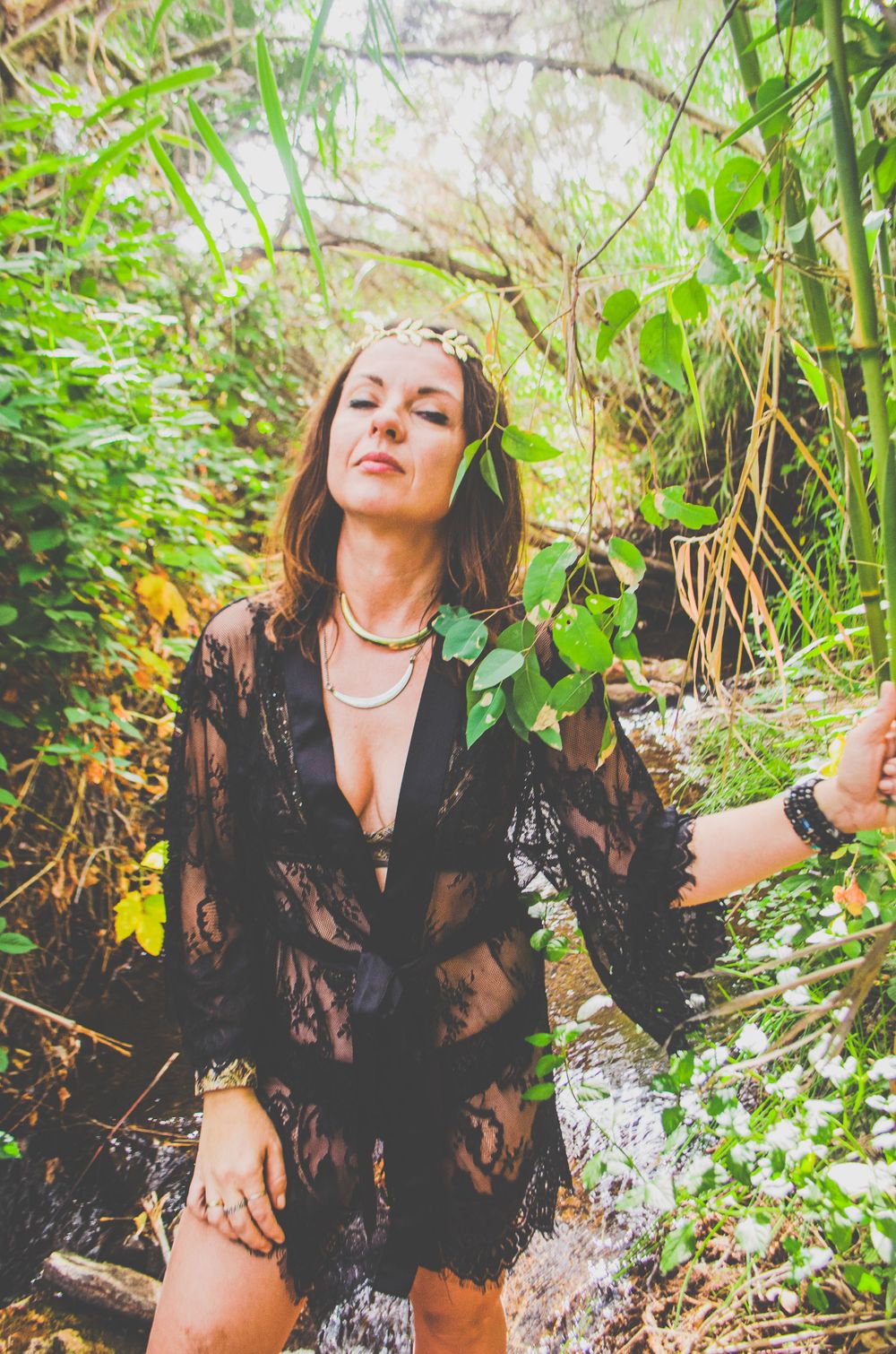 A portrait in nature featuring a black lace dress against lush green foliage and flowing water.
