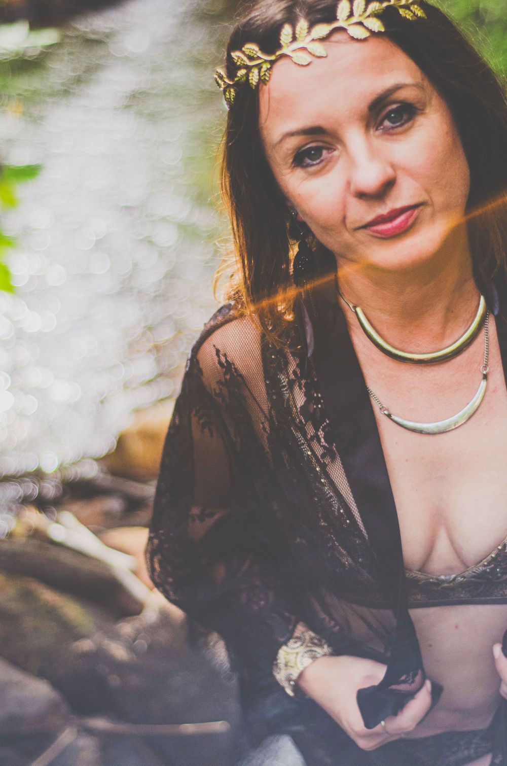 A bohemian-style portrait with a gold leaf crown and black lace ensemble in a natural setting.