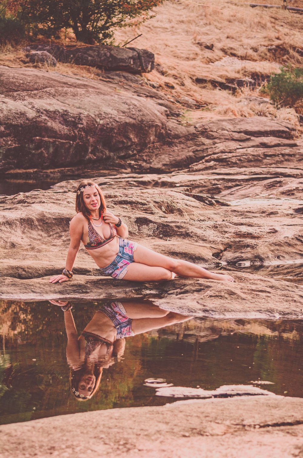 A model in a patterned swimsuit poses on red rocks beside a reflective pool.