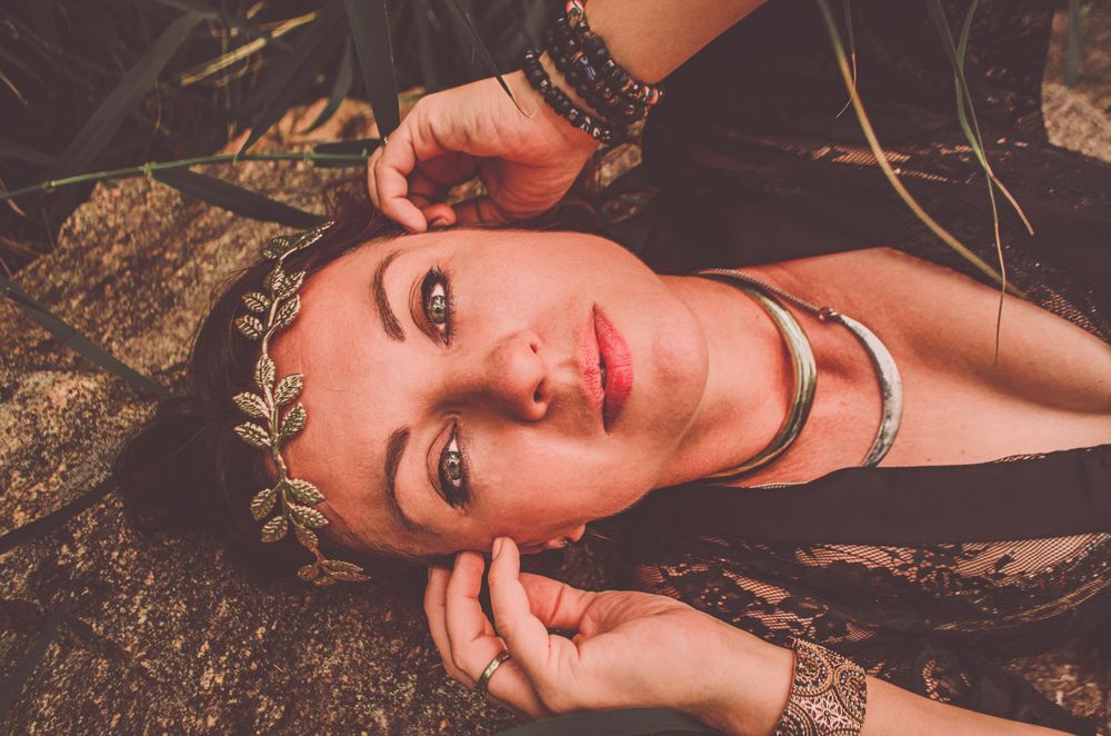 A close-up portrait with a gold leaf crown and silver necklace against natural textures.
