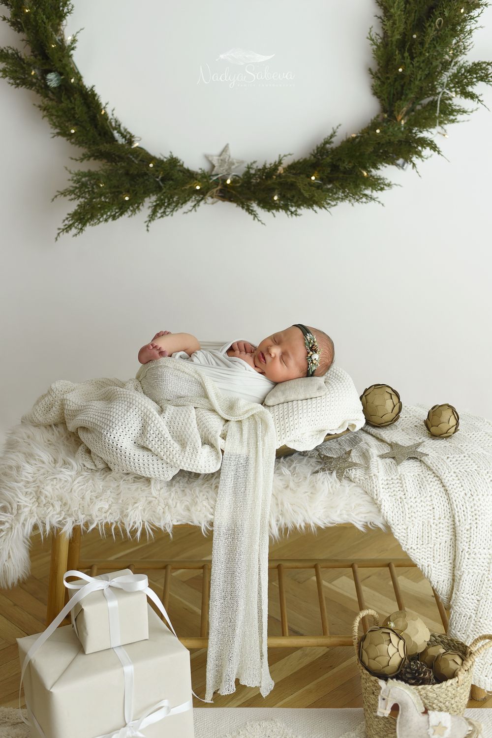 A series of five connected images showing a sleeping baby in white clothing on a cream colored surface with evergreen wreaths above.