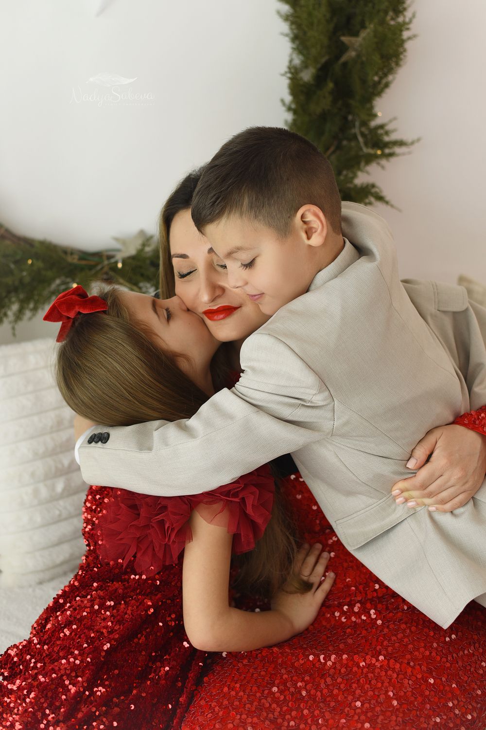 A tender holiday moment captured with a sparkling red dress and white suit against a festive backdrop.