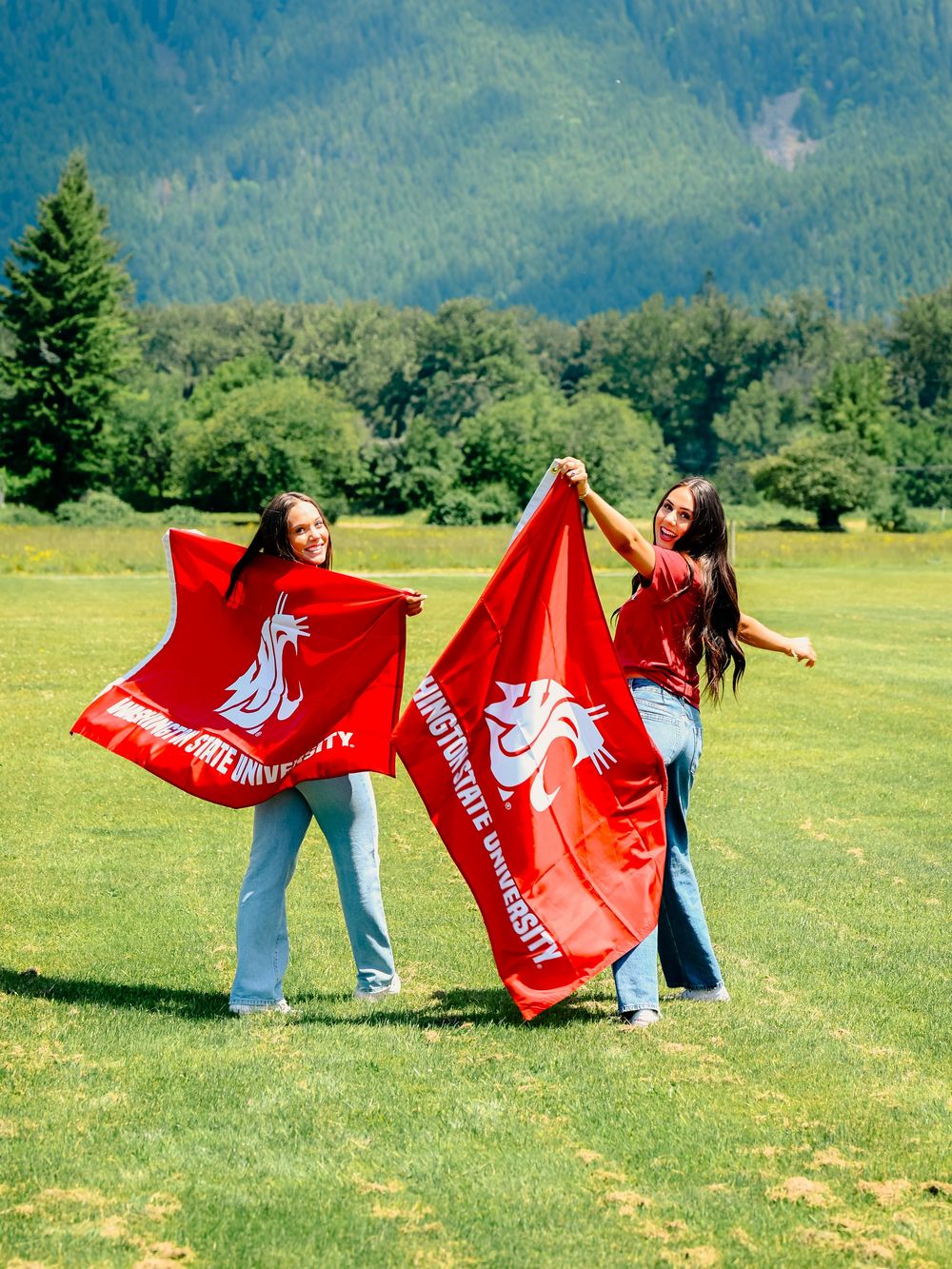 People wave red flags while posing in a grassy field with mountains in background.