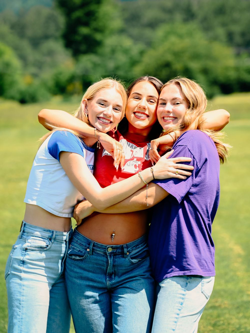 A group hugs and smiles while wearing coordinated outfits in a field.
