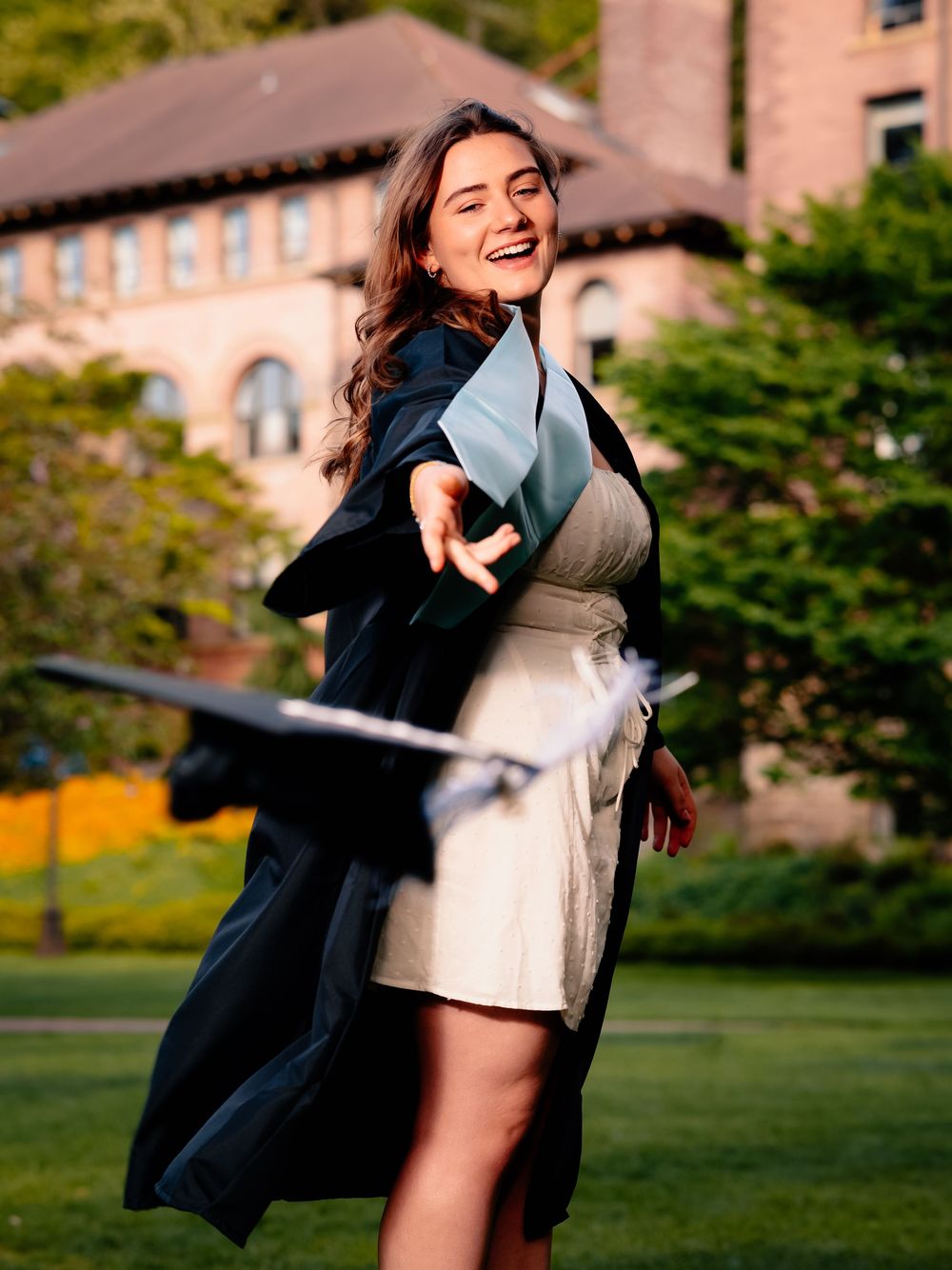 Celebratory graduation photoshoot with black gown and white dress on campus grounds.