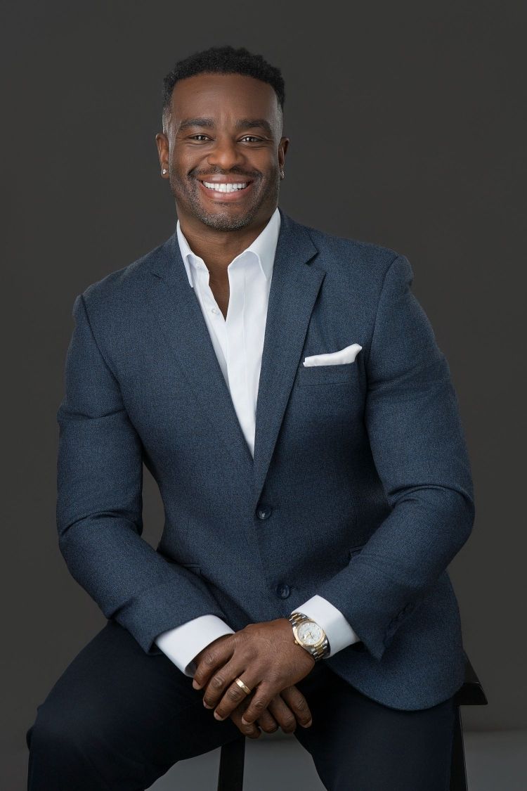 Professional headshot of person in white blouse with bow tie against grey backdrop.