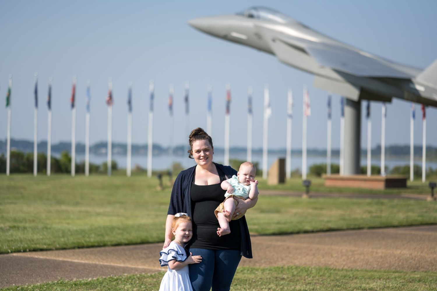 People stand on grassy area near aircraft display with row of international flags at outdoor aviation museum.