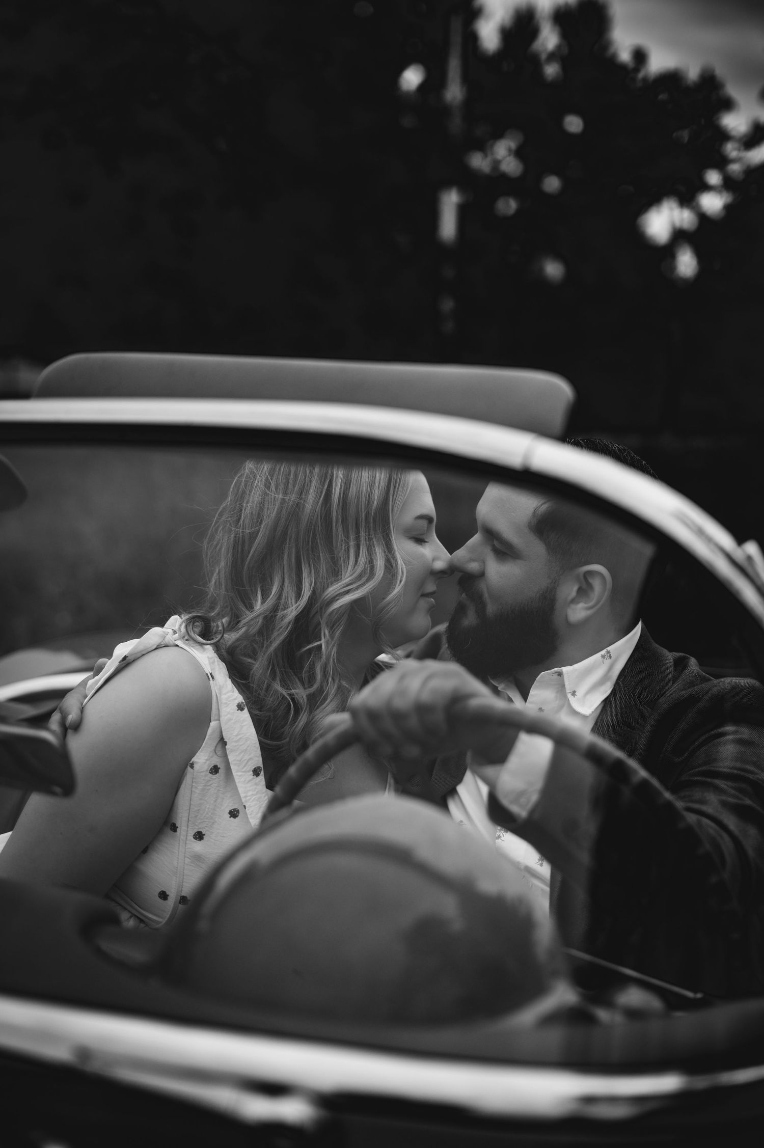A tender romantic moment captured in black and white showing a couple sharing a kiss inside a vintage car.