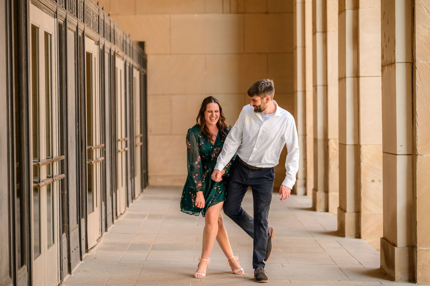 People walk through a stone colonnade hallway with arched columns and natural lighting casting shadows on the floor.