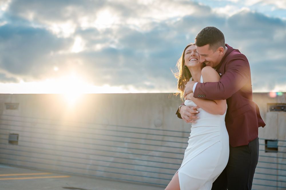 A couple embraces during their wedding photoshoot at sunset with dramatic cloudy skies in the background.