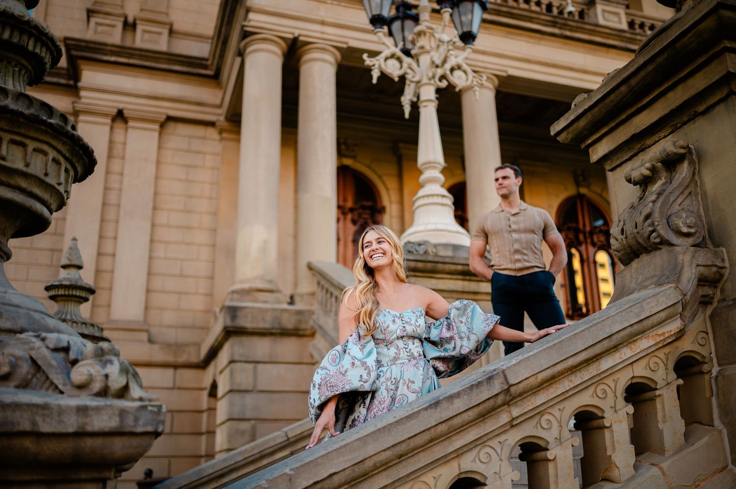 Elegant couple poses on grand staircase of historic mansion during sunset golden hour.