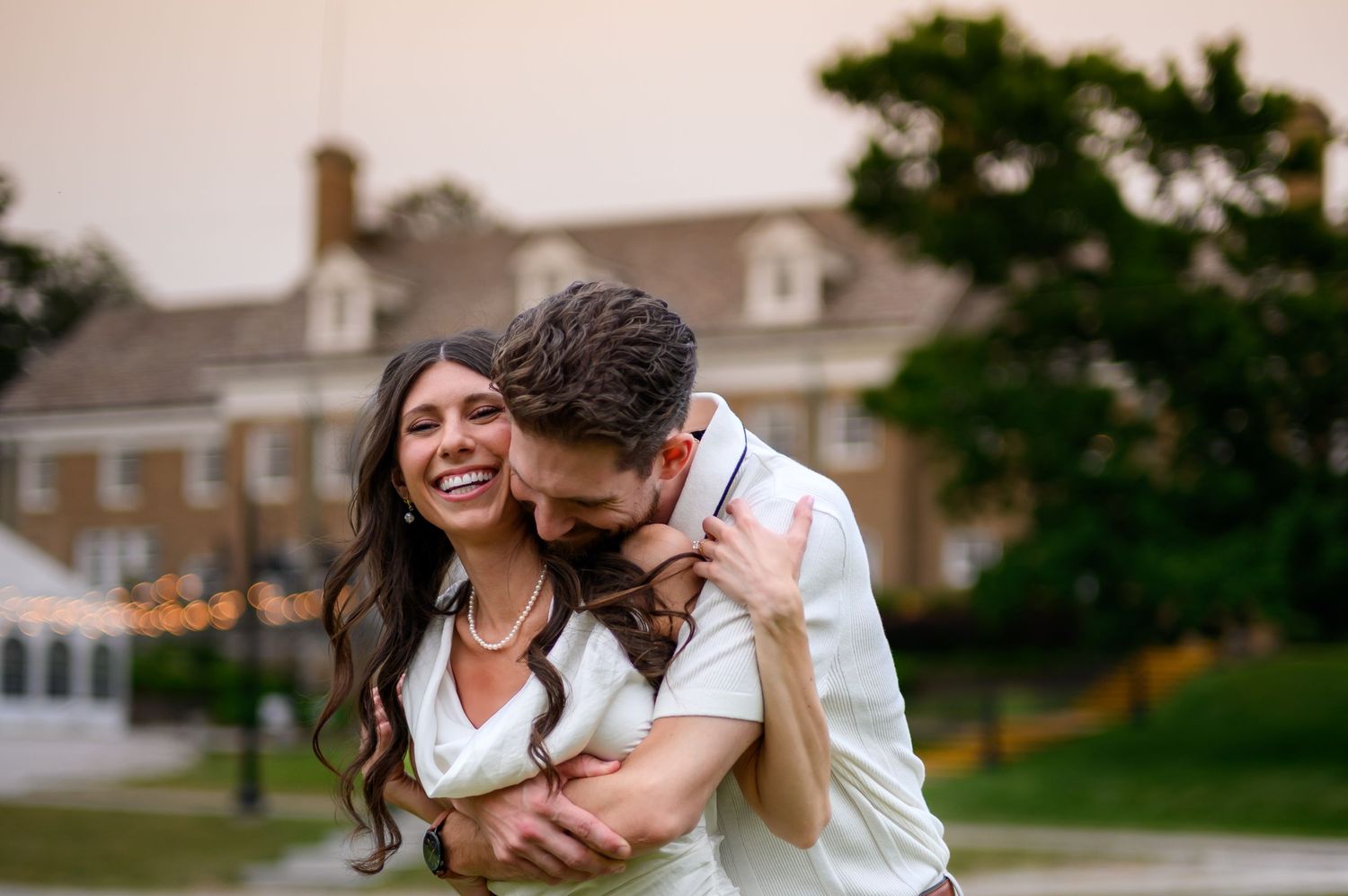 A happy couple embraces and laughs together in front of the stately Felt Mansion with a manicured lawn