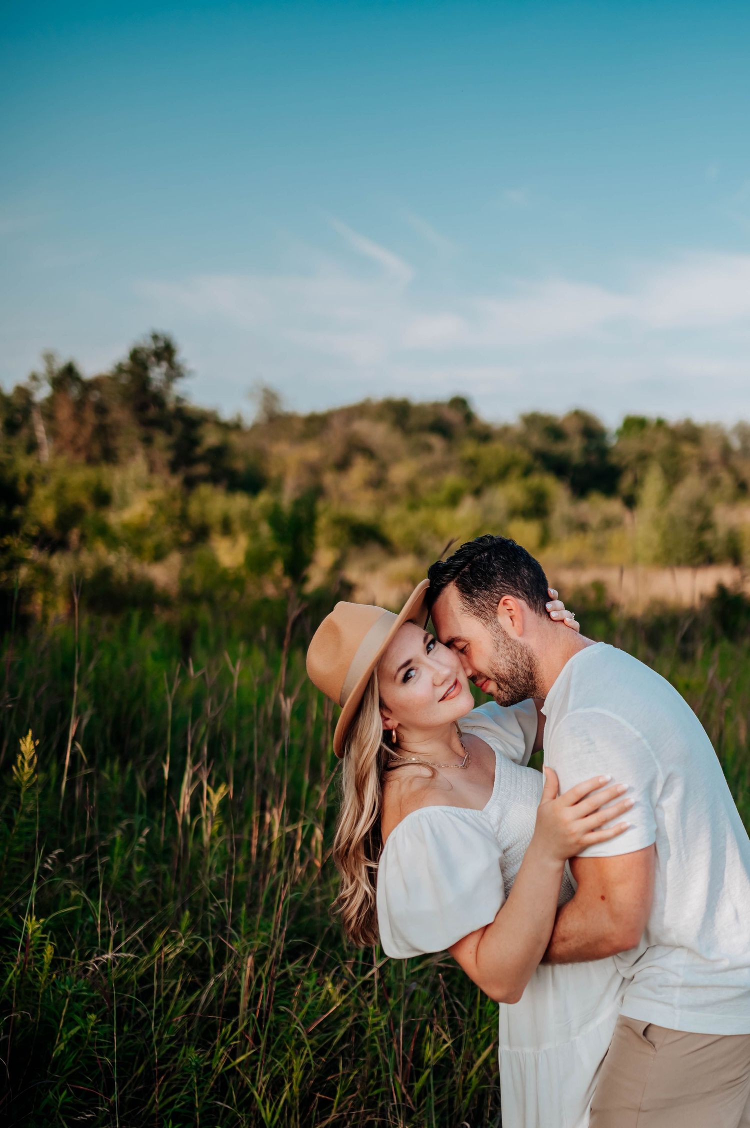 Couple shares an intimate moment in a golden field during sunset with a clear blue sky backdrop.