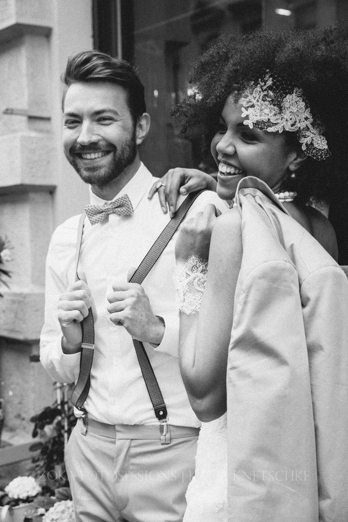 Black and white photo of a happy interracial bride and groom sharing a candid moment together in vintage-inspired attire.