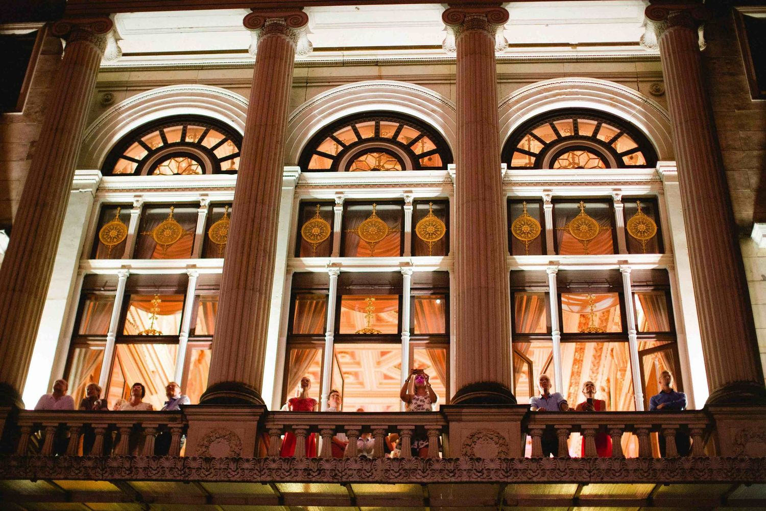 Illuminated arched windows of an elegant historic building at night with warm glowing lights streaming through.