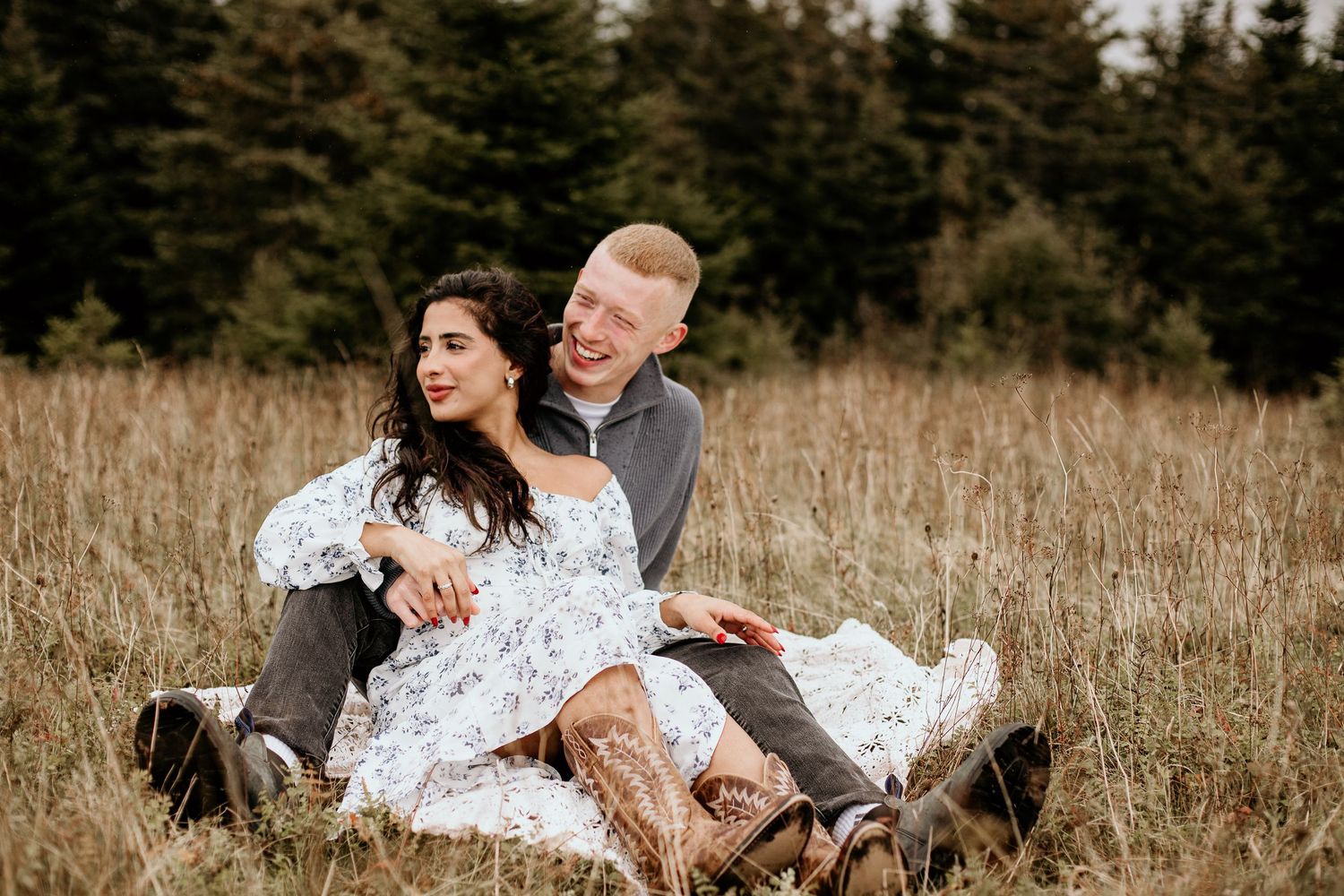 woman sitting in between man's legs cuddling in a field