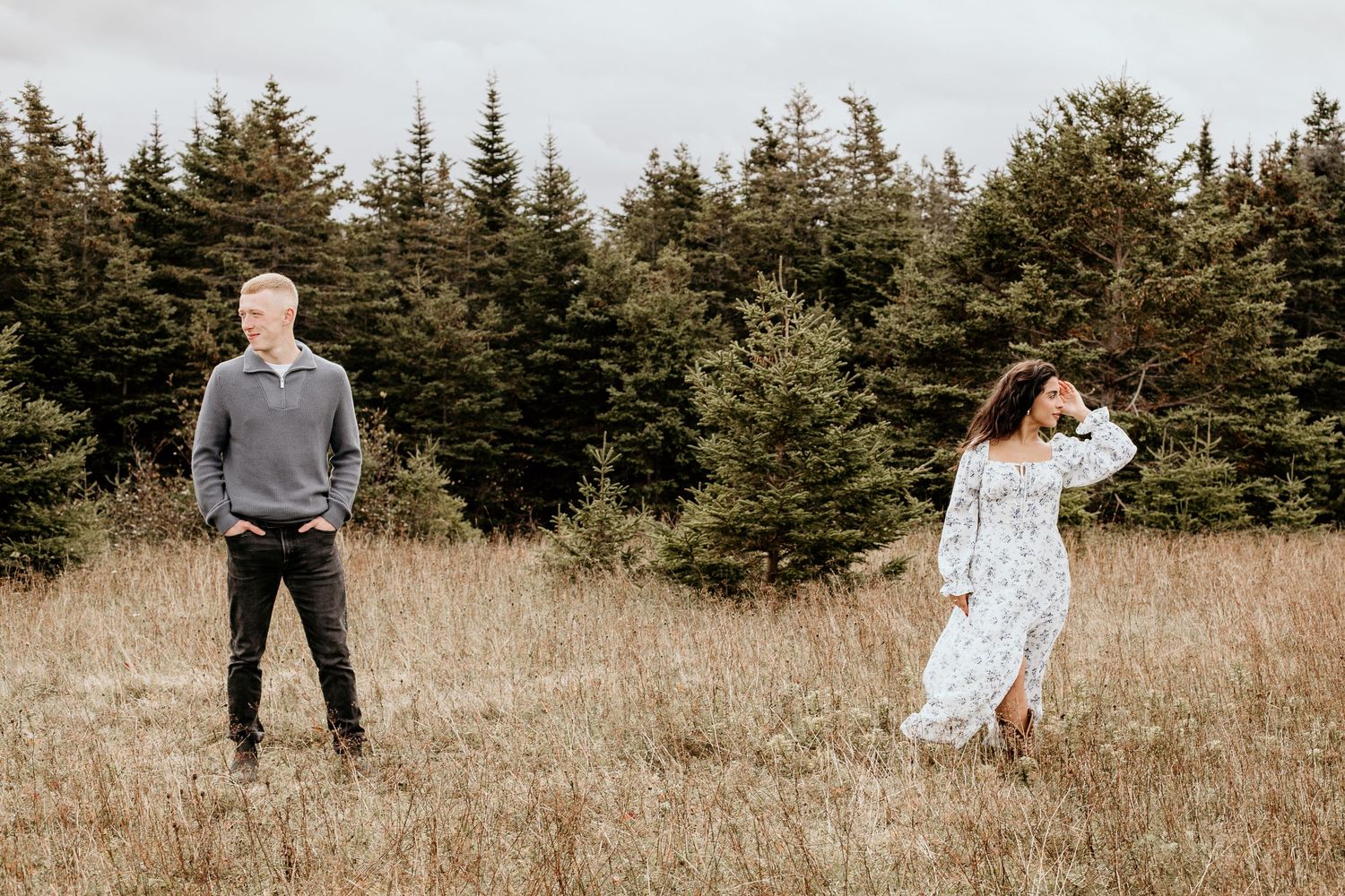couple standing apart from each other in brown field with trees behind them, looking in opposite directions