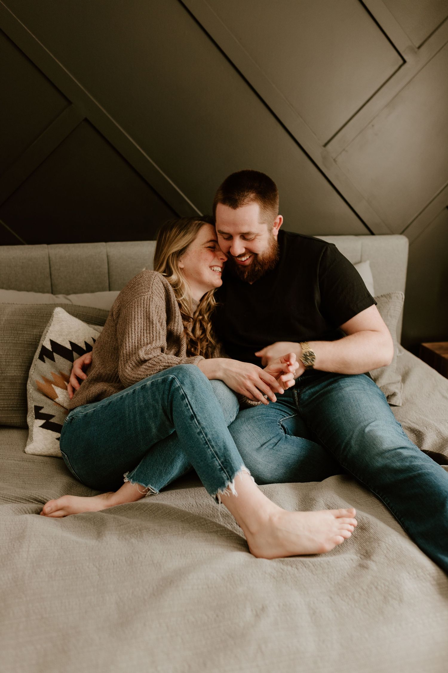 married couple in jeans cuddling on a bed laughing