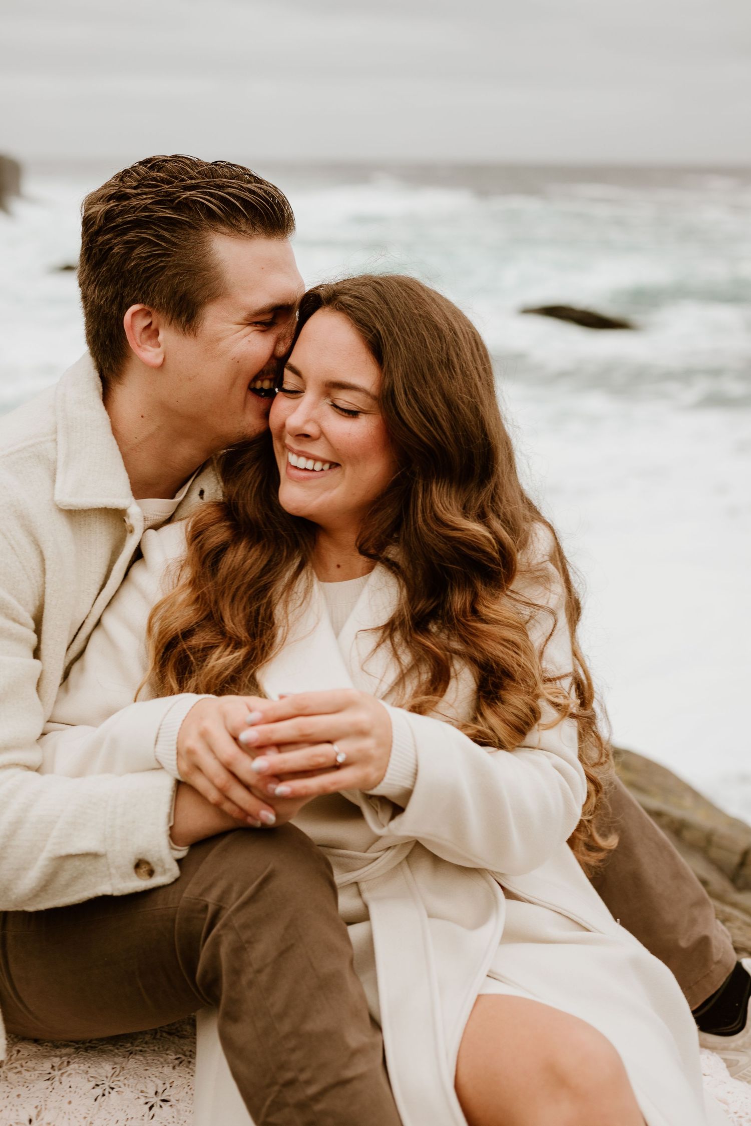 man whispering into fiance's ear while holding hands on a rocky Newfoundland beach