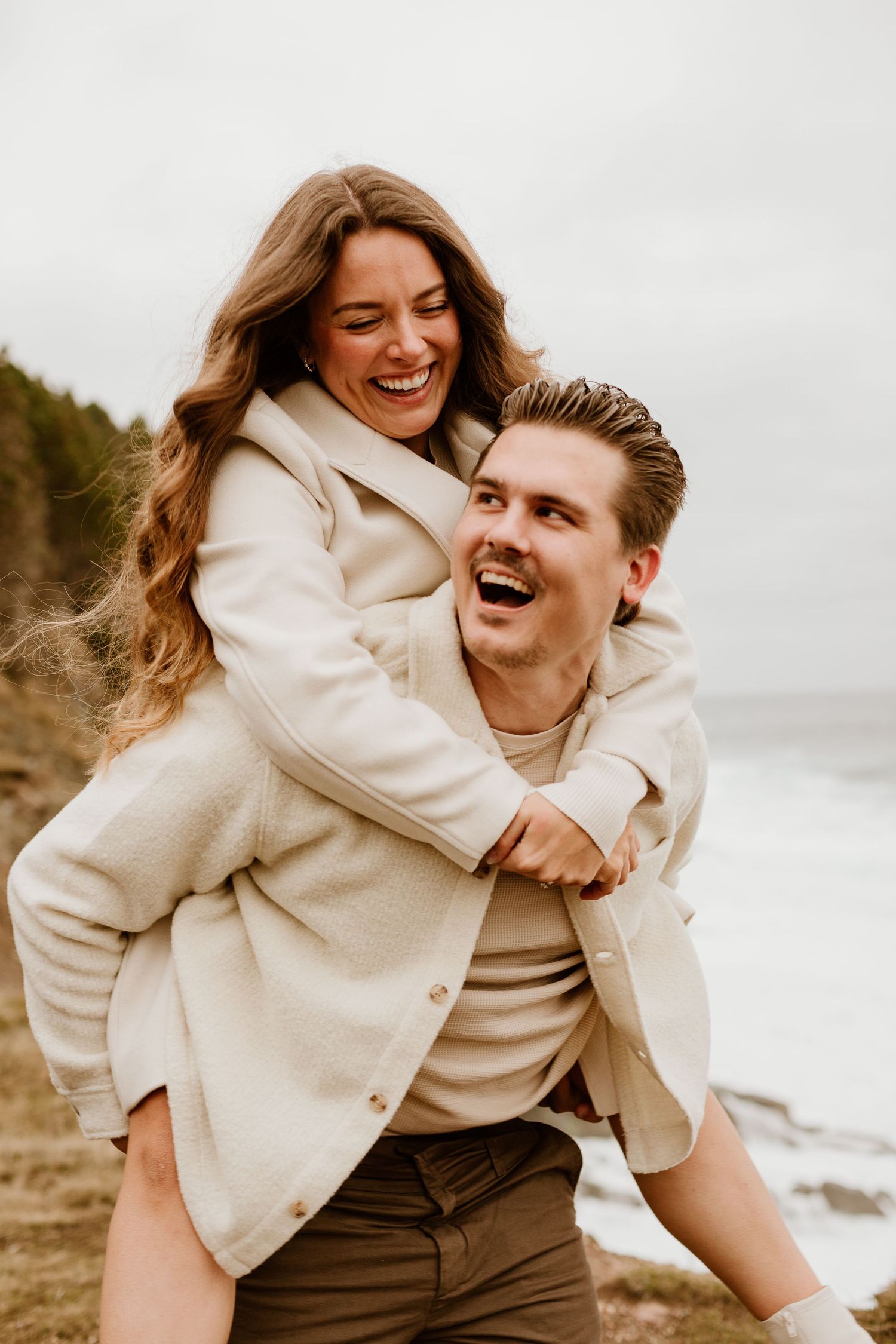 man giving his fiance a piggy back ride on the beach of Newfoundland