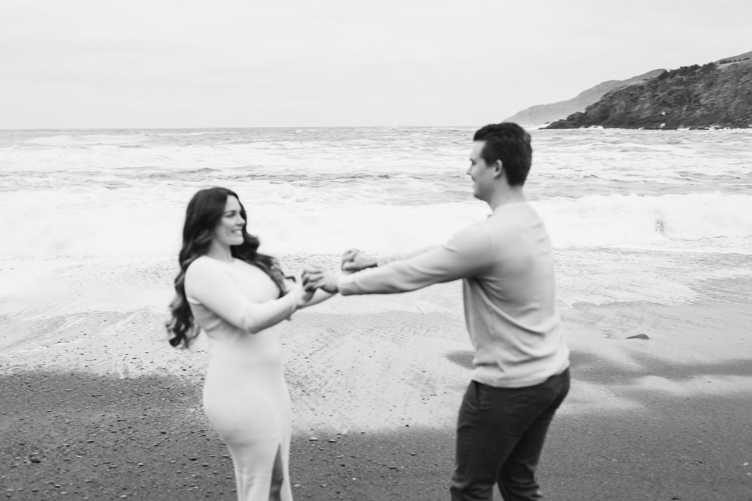 engaged couple holding hands and swinging around together on the beach