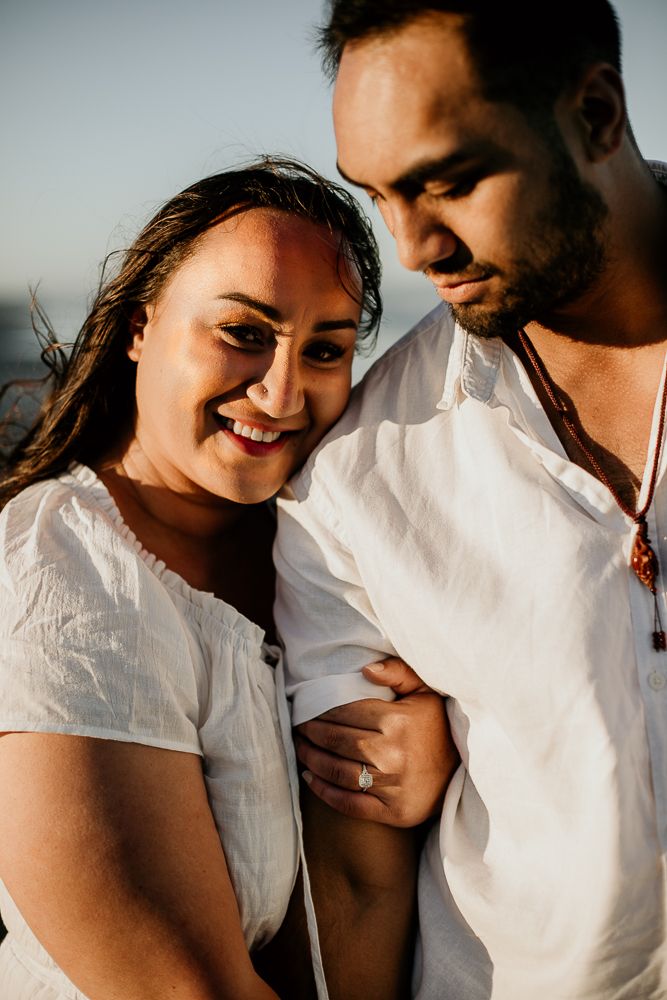 woman leaning on fiance's shoulder while smiling at the camera, man looking down at his fiance