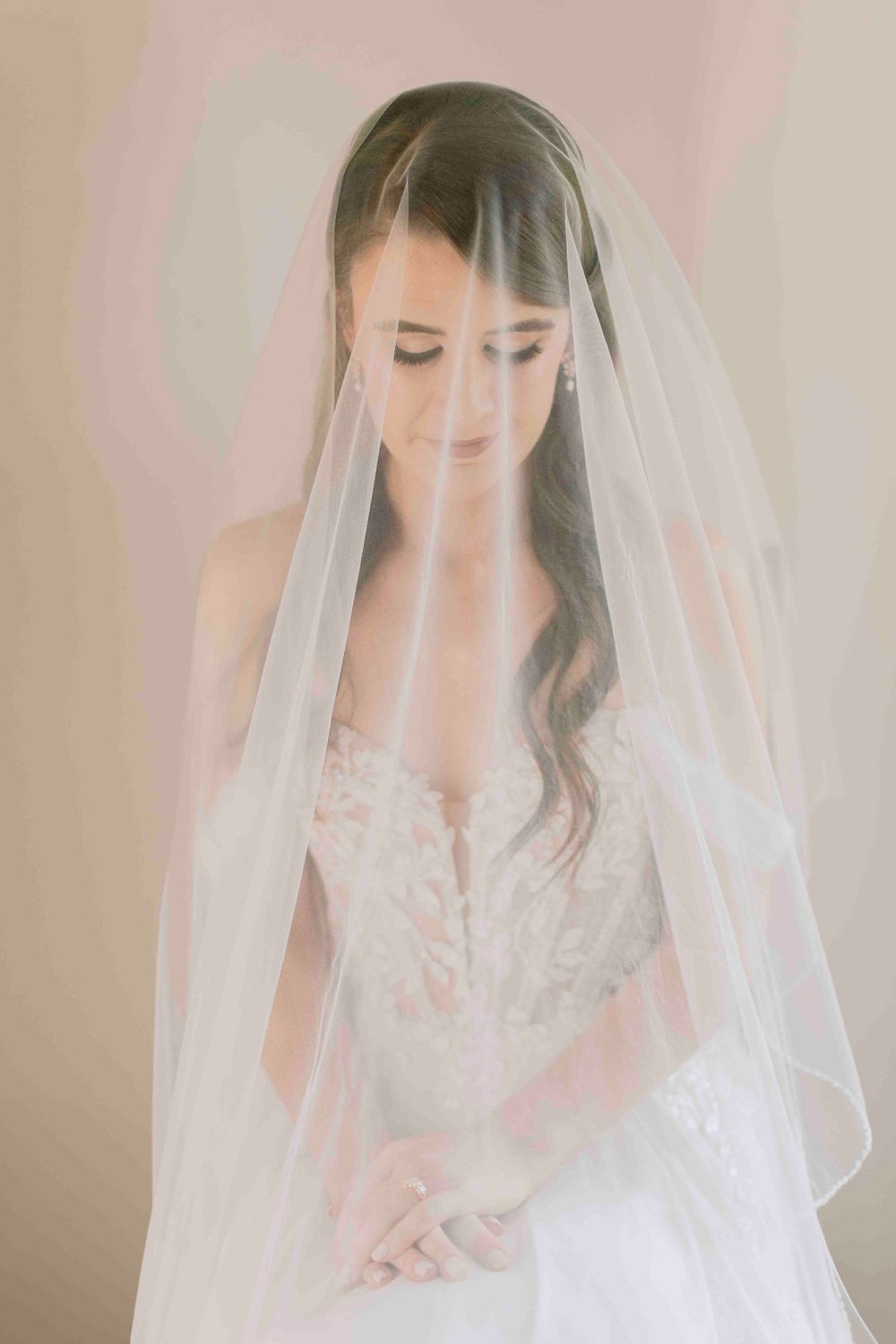 Elegant bride in lace wedding dress with long veil looking down peacefully.