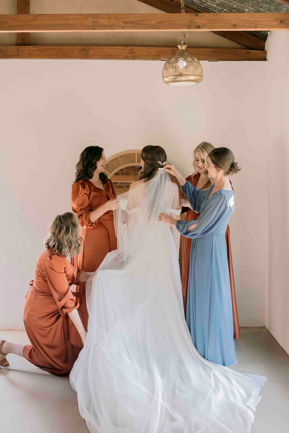 Bridesmaids in mixed rust and blue dresses arranging bride's cathedral veil.