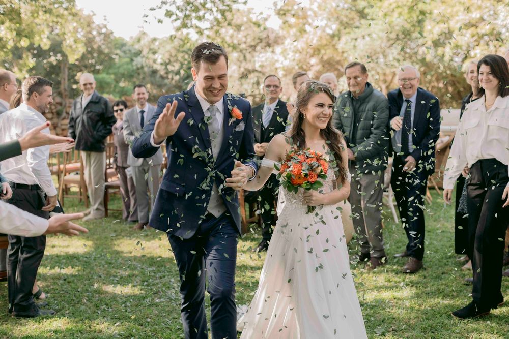 Joyful newlyweds walk through confetti shower as guests celebrate their outdoor garden wedding ceremony.