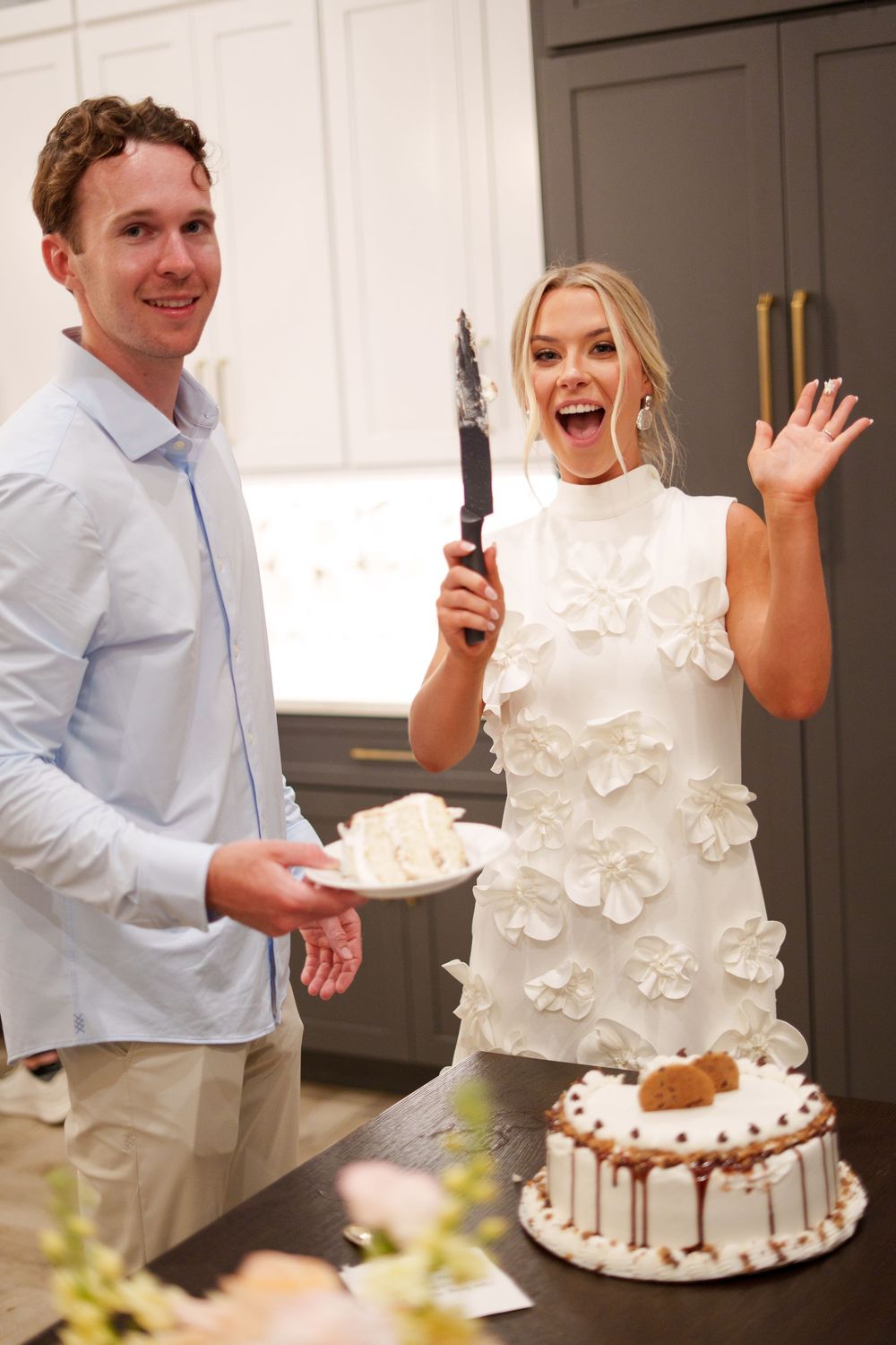 A couple celebrates with a bundt cake during a festive cake cutting moment in their white decorated kitchen.