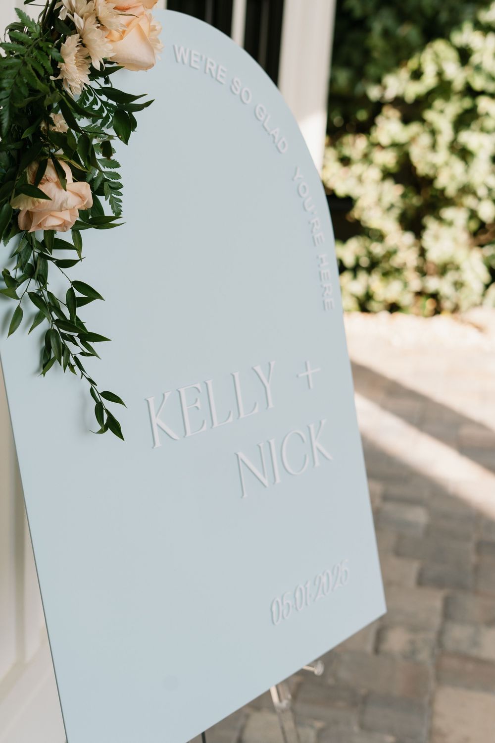 Close-up view of a light blue wedding seating chart styled like a tombstone with floral decorations in the corner.