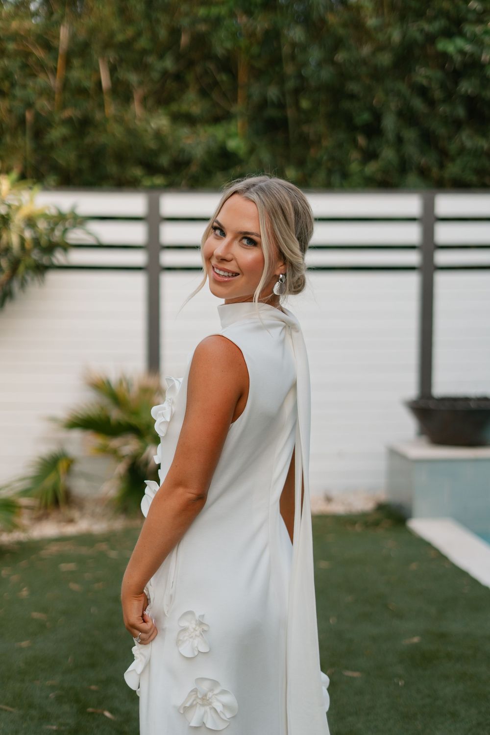 Someone in a white wedding dress with a cape-like overlay poses in a garden setting while showing details of the gown.