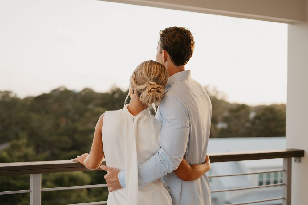 Couple embraces while enjoying sunset view from their balcony overlooking trees and nature.