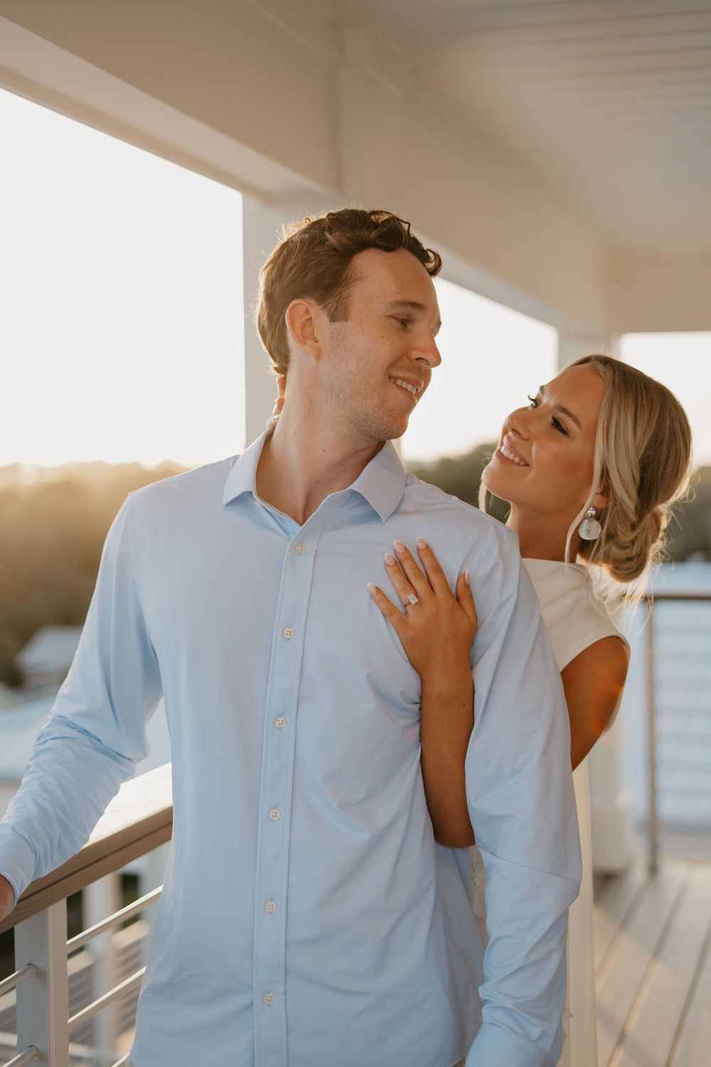 A couple shares a joyful moment together on a sunlit deck during their engagement shoot.