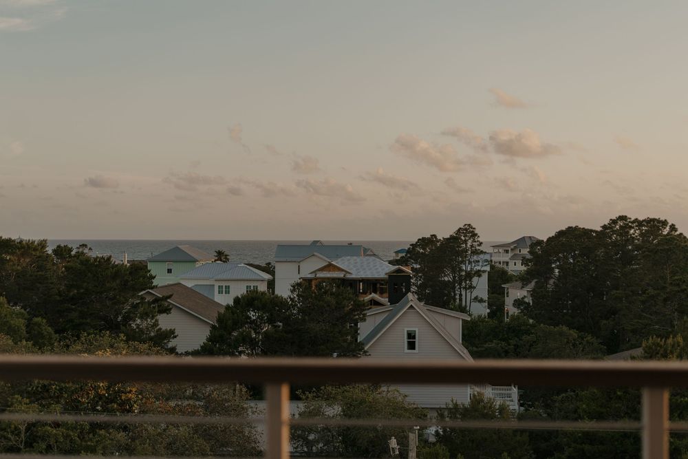 Coastal beach houses and cottages nestled among trees at sunset with pink-tinged clouds in the sky.