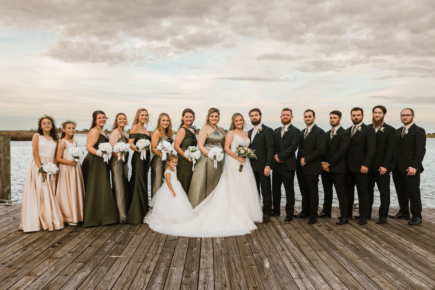 Wedding party poses together on wooden pier in Apalachicola Florida with natural cloudy sky backdrop. Wedding Photographer
