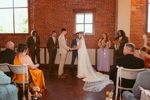 Wedding ceremony taking place in a rustic brick venue with natural light streaming through large windows.